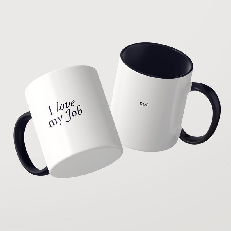 May include: Two white ceramic mugs with black interiors and black handles. One mug features the black text 'I love my Job' in a serif font, while the second mug displays the single word 'not.' in a smaller, simple black sans-serif font.