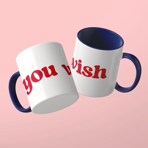 May include: Two white ceramic mugs with dark blue interiors and handles. The mugs feature the red text "you wish" printed in a bold, rounded, lowercase font. The mugs are positioned at an angle, displaying the text clearly against a light background.