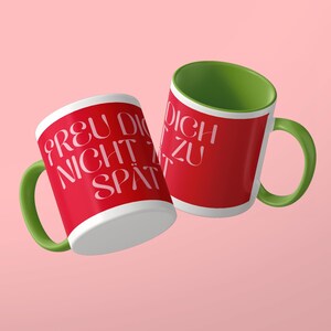 May include: Two ceramic mugs with a bright red exterior and a vibrant green interior and handle. The mugs feature white text that reads FREU DICH NICHT ZU SP&Auml;T in a stylized, rounded font. The design is consistent across both mugs.