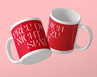 May include: Two white ceramic mugs with a bright red exterior finish. The mugs feature white text printed in a stylized font that reads "FREU DICH NICHT ZU SPÄT". Each mug has a curved handle on the side and a plain white interior surface.