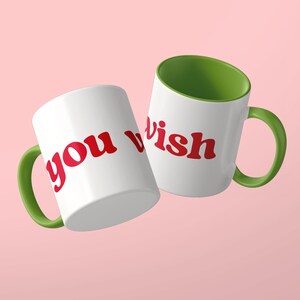 May include: Two white ceramic mugs with green interiors and green handles. The mugs feature the red text "you wish" printed in a bold, rounded font. The mugs are positioned at an angle, displaying the text clearly against the white exterior.