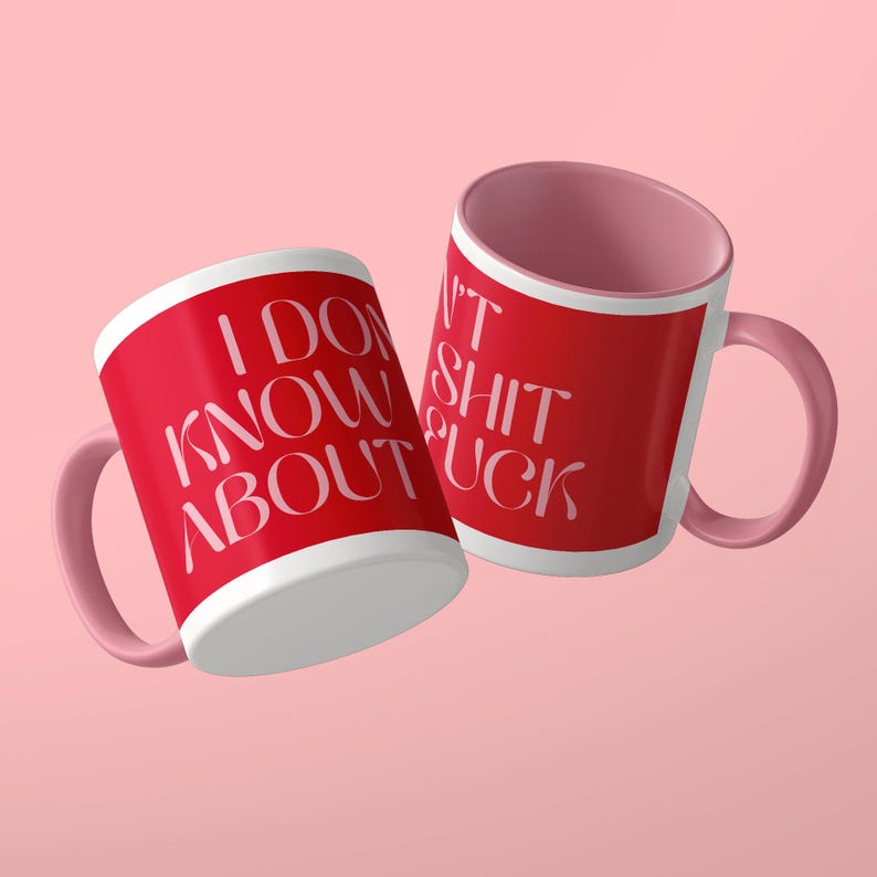 May include: Two ceramic mugs with a red exterior and a light pink interior and handle. The mug on the left features the white text I DON'T KNOW ABOUT. The mug on the right features the white text I DON'T SHIT FUCK in a stylized serif font.