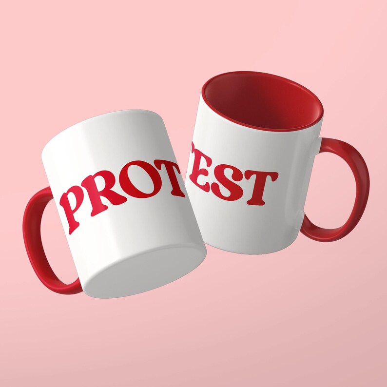 May include: Two white ceramic mugs with red interiors and red handles. The mug on the left features the red text PROT, while the mug on the right features the red text EST. Both mugs have a smooth, glossy finish and a standard cylindrical shape.