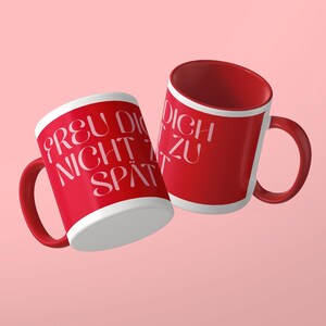 May include: Two ceramic mugs with a vibrant red exterior and white interior. The mugs feature the white text "FREU DICH NICHT ZU SP&Auml;T" printed in a stylized, elegant font. The handles are red, and the mugs are positioned at an angle.
