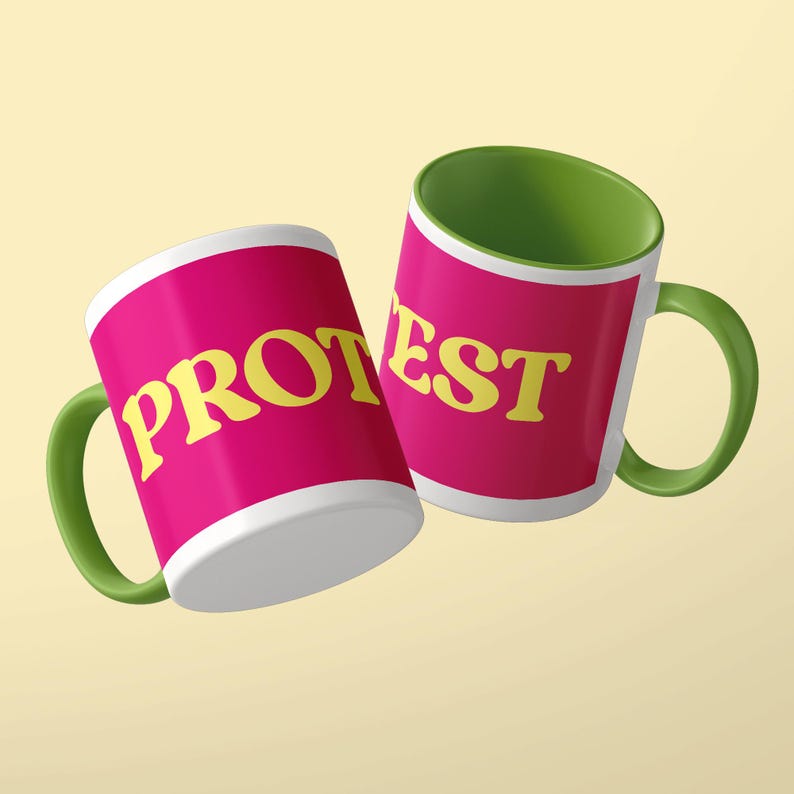 May include: Two ceramic mugs with a bright pink exterior and a green interior and handle. The mug on the left features the yellow text PROT, while the mug on the right displays the yellow text EST, completing the word PROTEST across both items.
