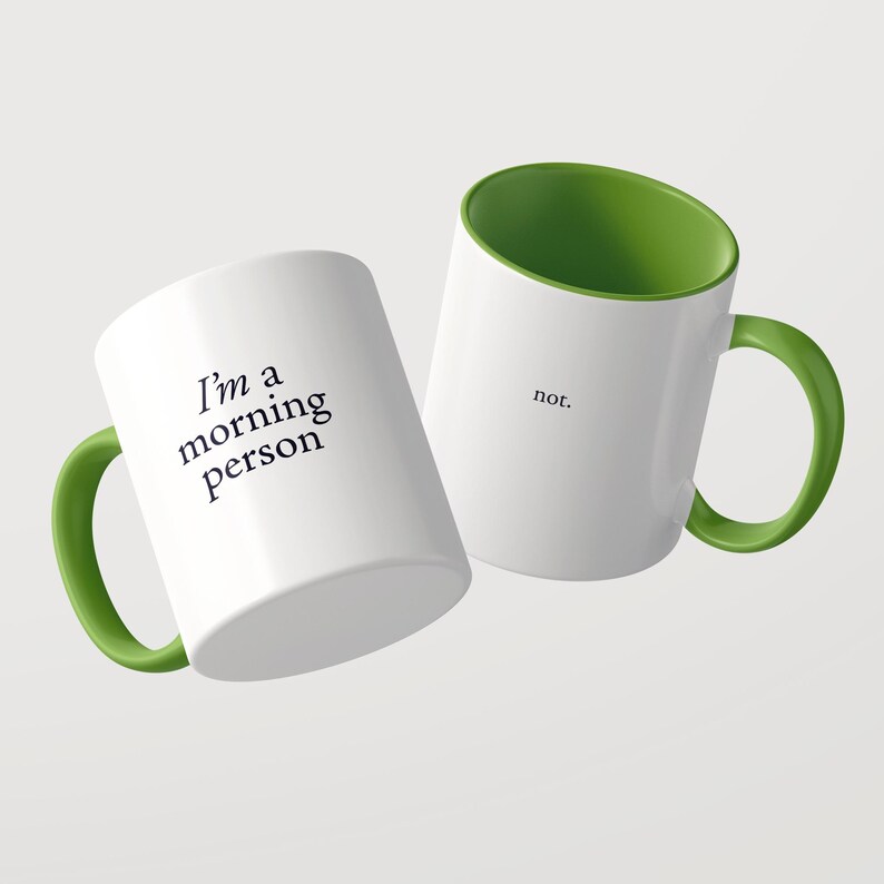 Może przedstawiać: Dwa białe ceramiczne kubki z jaskrawozielonym wnętrzem i uchwytem. Jeden kubek zawiera czarny napis "I'm a morning person", a drugi kubek zawiera czarny napis "not.". Kubki są ustawione pod kątem na jednolitym tle.