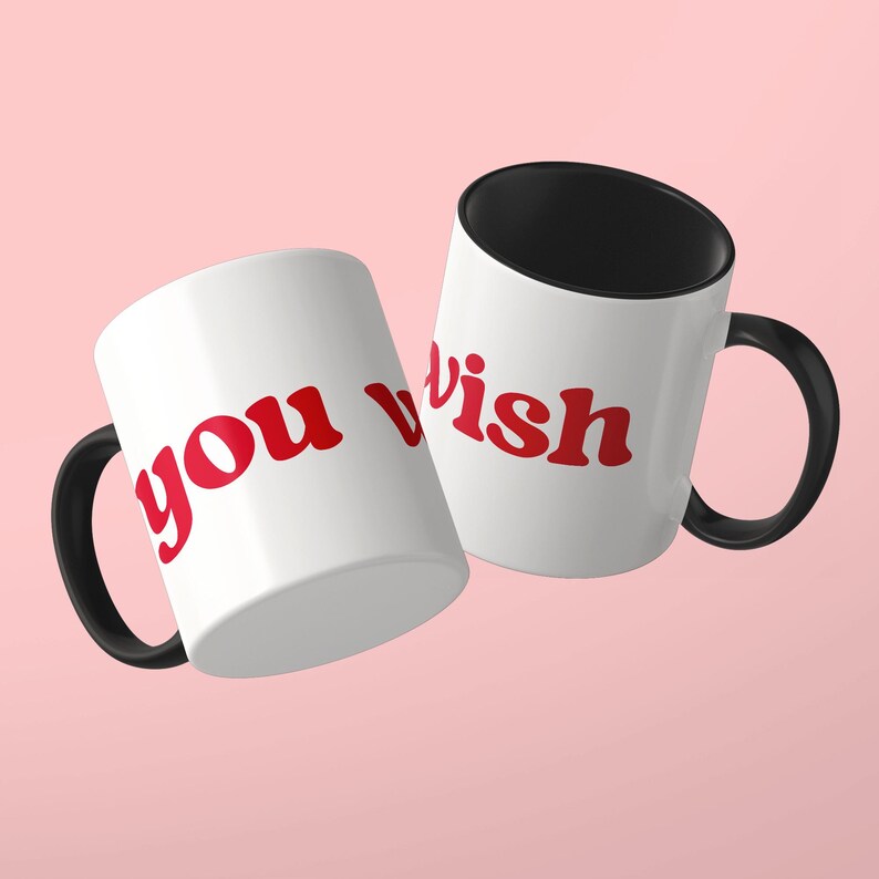 May include: Two white ceramic mugs with black handles and black interiors. The mugs feature the red text "you wish" printed in a bold, rounded font. The mugs are positioned at an angle, displaying the text clearly against the white exterior surface.