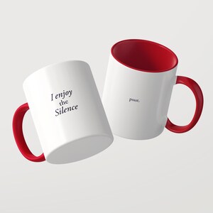 May include: Two white ceramic mugs with bright red interiors and matching red handles. One mug features the black text I enjoy the Silence, while the other mug displays the black text pssst. Both mugs have a smooth, glossy finish.