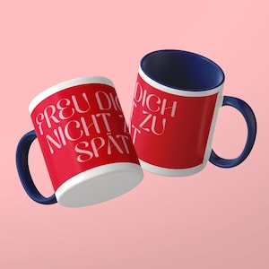 May include: Two ceramic mugs with a vibrant red exterior and a deep navy blue interior and handle. The mugs feature white text that reads FREU DICH NICHT ZU SP&Auml;T in a stylized serif font. The design is consistent across both mugs shown.