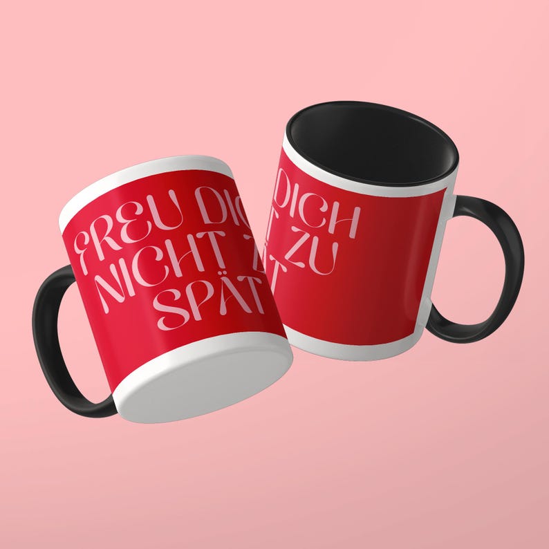 May include: Two ceramic mugs with a bright red exterior and a solid black interior and handle. The mugs feature white text printed on the red surface that reads "FREU DICH NICHT ZU SP&Auml;T" in a stylized, elegant serif font with curved lettering.