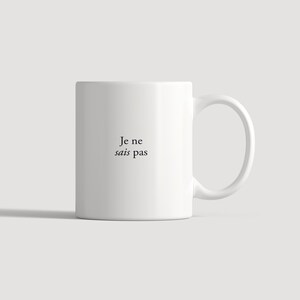 May include: A white ceramic mug featuring a side handle and the black printed text Je ne sais pas centered on the front. The mug has a smooth, cylindrical body and a clean, minimalist design suitable for holding hot or cold beverages.