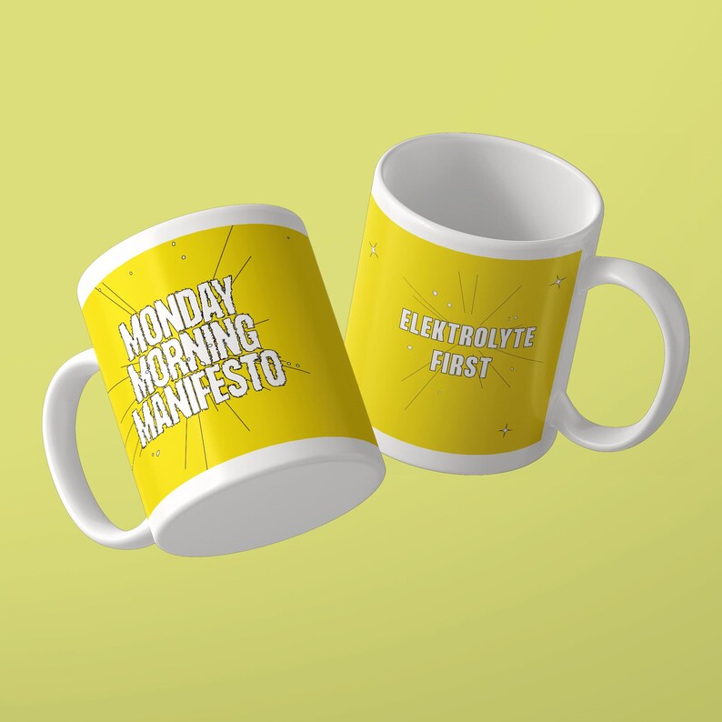 May include: Two white ceramic mugs with yellow exterior surfaces. One mug features the black text MONDAY MORNING MANIFESTO with radiating lines. The other mug displays the white text ELEKTROLYTE FIRST with radiating lines and small star accents.