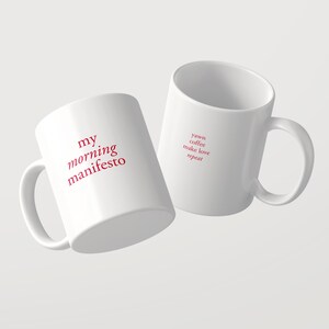 以下が含まれることがあります： 赤い文字がプリントされた2つの白いセラミック製マグカップ。1つには「my morning manifesto」というフレーズが太いセリフ体で書かれています。もう1つには「yawn coffee make love repeat」という小さな積み重ねられたテキストが同じ赤色とフォントスタイルで書かれています。