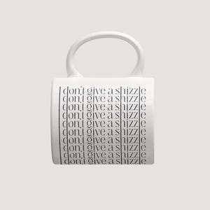 K&ouml;nnte beinhalten: Ein wei&szlig;er Keramikbecher mit einem gro&szlig;en, abgerundeten Henkel und einem sich wiederholenden schwarzen Textdesign. Der Satz "i don't give a shizzle" ist in einer d&uuml;nnen, serifenlosen Schrift neunmal vertikal auf der Vorderseite des Bechers gedruckt.