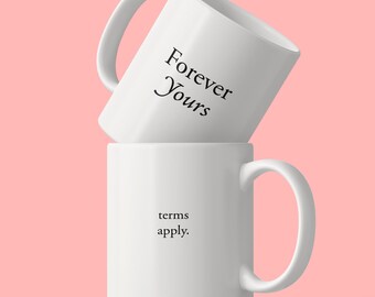 May include: Two white ceramic mugs stacked vertically. The top mug is tilted and features the black text Forever Yours. The bottom mug is upright and features the black text terms apply. Both mugs have a smooth finish and a single side handle.