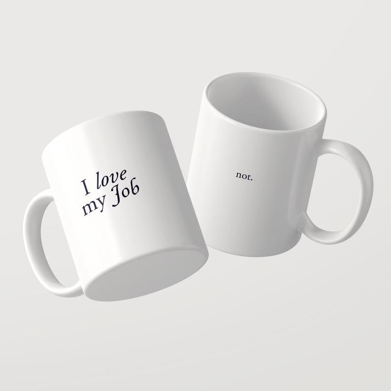 May include: Two white ceramic mugs with black text. One mug features the phrase "I love my Job" in a serif font, while the second mug displays the word "not." in a smaller, simple font. Both mugs have a standard handle and cylindrical shape.