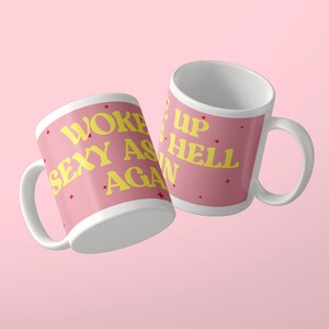 Może przedstawiać: Dwa białe kubki ceramiczne z r&oacute;żową powierzchnią zewnętrzną i ż&oacute;łtym napisem WOKE UP SEXY AS HELL AGAIN. Projekt zawiera małe czerwone gwiazdki rozrzucone na r&oacute;żowej powierzchni, a napis biegnie wok&oacute;ł obu kubk&oacute;w.