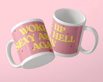 May include: Two white ceramic mugs with a pink exterior featuring yellow text that reads WOKE UP SEXY AS HELL AGAIN. The design includes small red star accents scattered across the pink surface, with the text wrapping around the mugs.
