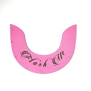 May include: A crescent-shaped piece of bright pink textured leather with small pre-punched holes along the curved edges. The text "Flash Me" is printed in a black, elegant cursive font across the centre of the pink leather material.