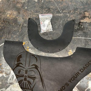 May include: Black leather components featuring a Darth Vader design and the text "WHO'S YOUR DADDY". A small bag of silver rivets is also present. These parts seem to be for a larger item.