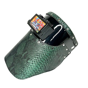 May include: A welding helmet with a green snakeskin pattern on the front and sides. The top is black and glossy. The helmet has a rectangular viewing window with the words "KEEP IT CLASSY" on it.