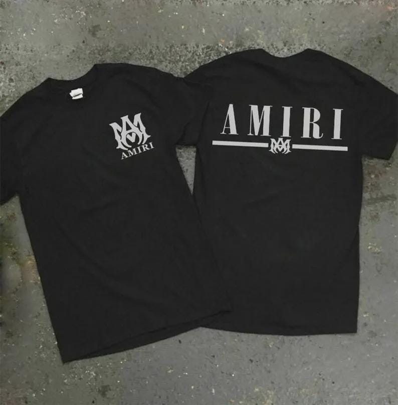 Puede incluir: Dos camisetas negras con la palabra "AMIRI" impresa en blanco. Una camiseta tiene el logotipo y el texto en la parte delantera, y la otra tiene el texto y el logotipo en la parte trasera. Las camisetas est&aacute;n hechas de un material suave.