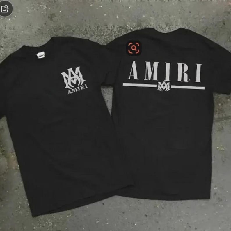 Puede incluir: Dos camisetas negras con la palabra "AMIRI" impresa en blanco. Una camiseta tiene el logo en la parte delantera y la otra en la trasera. Las camisetas son de manga corta y parecen estar hechas de un material suave.