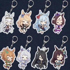May include: Eight anime-style character keyrings with silver metal clasps. Each keyring features a different character with unique hair colours and outfits. The characters have large eyes and are smiling. The keyrings are on a dark blue background.