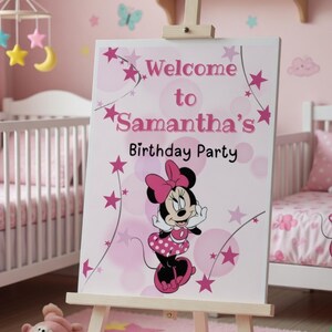 May include: A pink and white sign on an easel reads "Welcome to Samantha's Birthday Party" with a Minnie Mouse graphic. The sign is in a pink room with a crib and Minnie Mouse bedding.