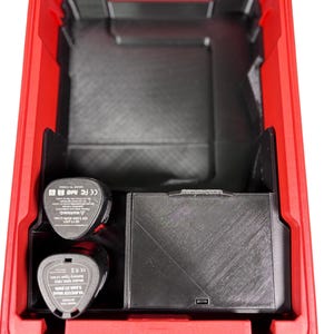 Puede incluir: Maleta de herramientas de plástico rojo con compartimentos interiores negros. Dos baterías negras y una caja de almacenamiento negra son visibles en el interior. La maleta está abierta, revelando la organización interna.