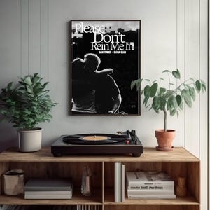 Puede incluir: Un grabado en blanco y negro enmarcado con el texto "Please Don't Rein Me In" sobre una silueta de dos personas abraz&aacute;ndose. Un tocadiscos con un disco de vinilo est&aacute; sobre una estanter&iacute;a de madera, con plantas en macetas.