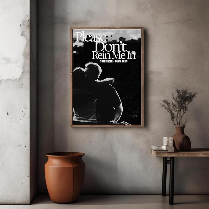 Puede incluir: Un cuadro en blanco y negro con el texto "Please Don't Rein Me In" y los nombres Sam Fender y Olivia Dean. La imagen muestra a dos personas abraz&aacute;ndose. El cuadro est&aacute; colgado en una pared gris.