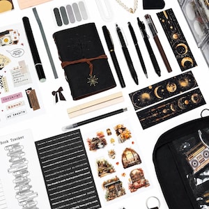 May include: A collection of stationery items including a black leather-bound journal with a ship wheel charm, various black pens, celestial-themed bookmarks, sticker sheets with autumn illustrations, a book tracker list, and a black zippered pouch.