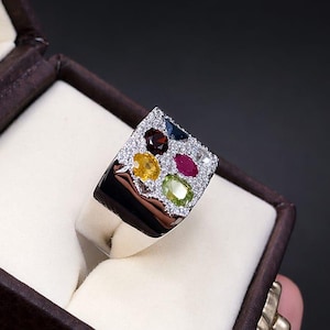 May include: A silver ring with a rectangular face set with various coloured gemstones and small white diamonds. The ring is displayed in a brown jewellery box. The word "SILVERISTRY" is at the top of the image.