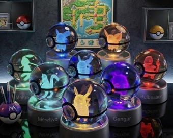 Peut inclure: Une collection de lampes sphériques en verre avec des figurines Pokemon gravées au laser en 3D, reposant sur des bases circulaires étiquetées avec des noms comme Pikachu, Mewtwo, Gengar et Bulbasaur. Une affiche Pokemon Kanto Region Trainer Map est suspendue derrière.