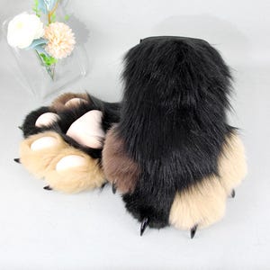 May include: A pair of plush animal paw gloves featuring long black faux fur on the top, tan faux fur on the fingers, and rounded light pink pads on the palms. Each finger is tipped with a sharp, glossy black claw for a realistic creature effect.