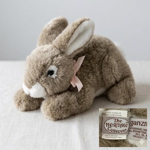May include: A plush, brown rabbit with long ears and a pink ribbon around its neck. The stuffed animal has white accents on its face and ears. The Heritage Collection tag is visible.