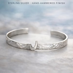 May include: A sterling silver cuff bracelet with a hand-hammered finish. The bracelet features a 'J' shaped design and the text "St. John's J Cuff Bracelet". The text "Classic. Authentic. Made to be worn." is also visible.