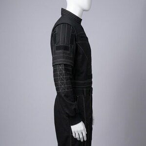 K&ouml;nnte beinhalten: Schwarzer Overall mit wei&szlig;en Steppdetails. Er hat einen hohen Kragen, lange &Auml;rmel mit geometrischen N&auml;hten und eine taillierte Silhouette. Der Overall hat einen G&uuml;rtel und Taschen. Das Design ist modern und elegant.