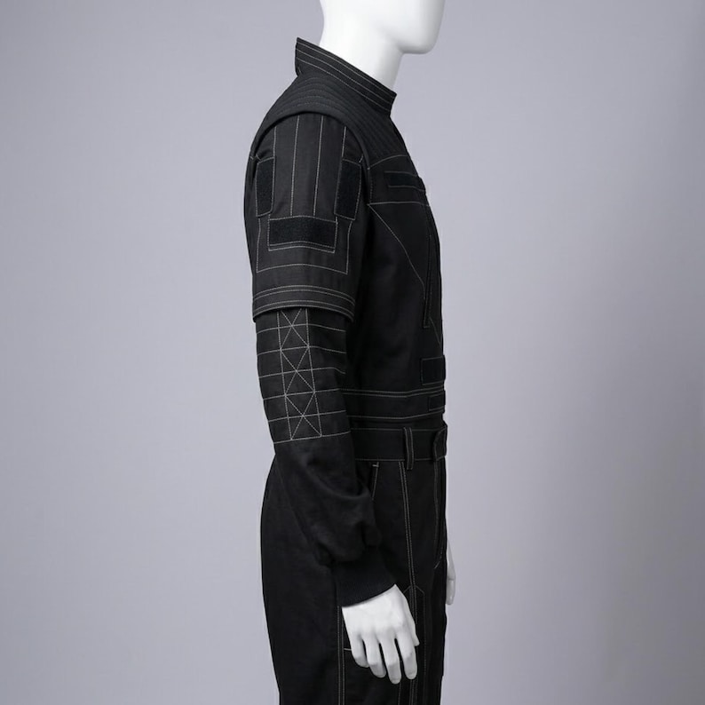K&ouml;nnte beinhalten: Schwarzer Overall mit wei&szlig;en Steppdetails. Er hat einen hohen Kragen, lange &Auml;rmel mit geometrischen N&auml;hten und eine taillierte Silhouette. Der Overall hat einen G&uuml;rtel und Taschen. Das Design ist modern und elegant.