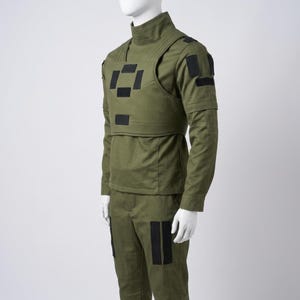 May include: Olive green tactical uniform displayed on a mannequin. The outfit includes a high-neck shirt, a vest with black square patches, and matching pants. The uniform has long sleeves and is designed for functionality.