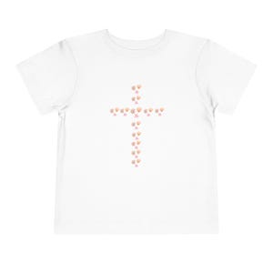 May include: White toddler t-shirt featuring a cross design made of seashells and pink starfish. The cross is centered on the front of the shirt. The shirt is made of a soft, comfortable material.