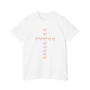 May include: White t-shirt featuring a cross design made of seashells and starfish. The cross is centered on the shirt, with the seashells in shades of tan and the starfish in pink. The shirt has short sleeves and a crew neck.