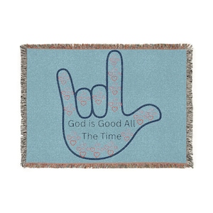 May include: A light blue woven throw blanket featuring a dark blue outline of a hand making the American Sign Language sign for I love you. The hand shape is filled with small red heart outlines and the text God is Good All The Time.