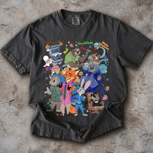 Op de afbeelding: Donkergrijs t-shirt met een kleurrijke cartoonillustratie van verschillende dierenfiguren. Het ontwerp bevat personages als een vos, konijn, luiaard en anderen, met tekstlabels. Het shirt is gemaakt van een zacht materiaal.