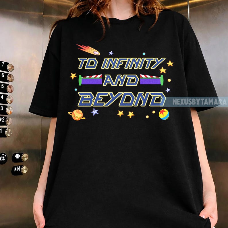 May include: Black t-shirt featuring the phrase "TO INFINITY AND BEYOND" in a colorful, stylized font. The design includes stars, a planet, and a shooting star, evoking a space theme. The shirt is a casual wear item.