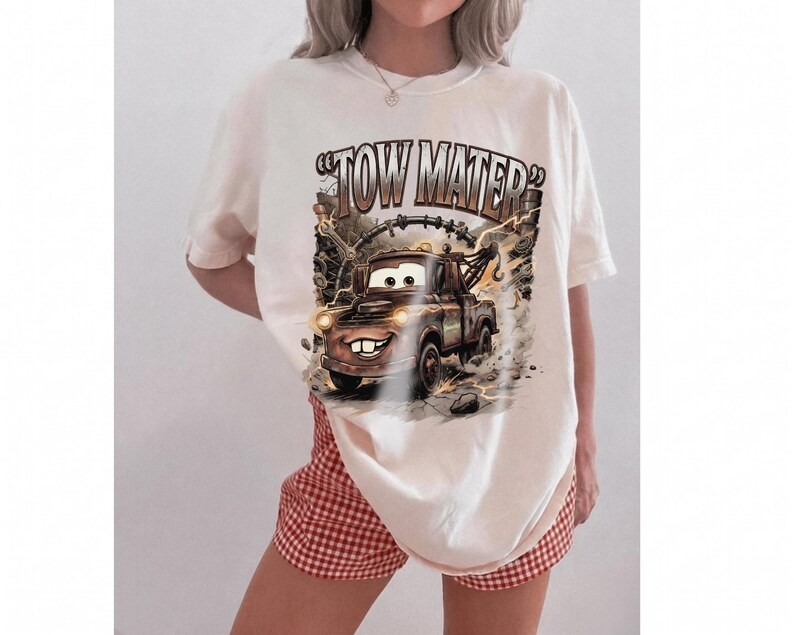 May include: Cream-colored t-shirt featuring a cartoon image of Tow Mater from the movie Cars. The graphic includes the text "Tow Mater" in a distressed font, with the character in action. The shirt is paired with red and white checkered shorts.