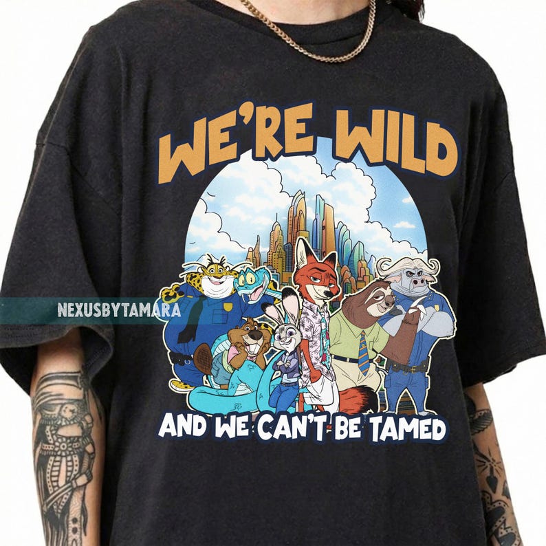 Puede incluir: Camiseta gris oscuro con un gr&aacute;fico colorido de personajes de la pel&iacute;cula animada Zootopia. El texto "WE'RE WILD AND WE CAN'T BE TAMED" est&aacute; impreso arriba y abajo de la imagen. La camiseta tiene cuello redondo y mangas cortas.