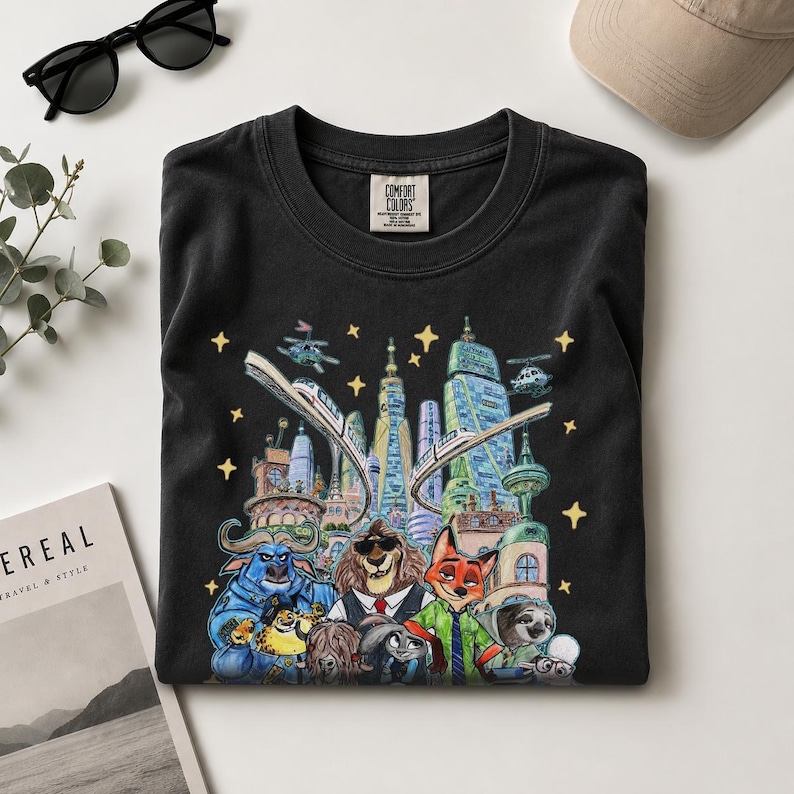 K&ouml;nnte beinhalten: Schwarzes Comfort Colors T-Shirt mit einer farbenfrohen Illustration einer Stadt mit Tierfiguren. Das Design umfasst einen Zug, Hubschrauber und Sterne. Das T-Shirt hat einen Rundhalsausschnitt und ein kleines Etikett.