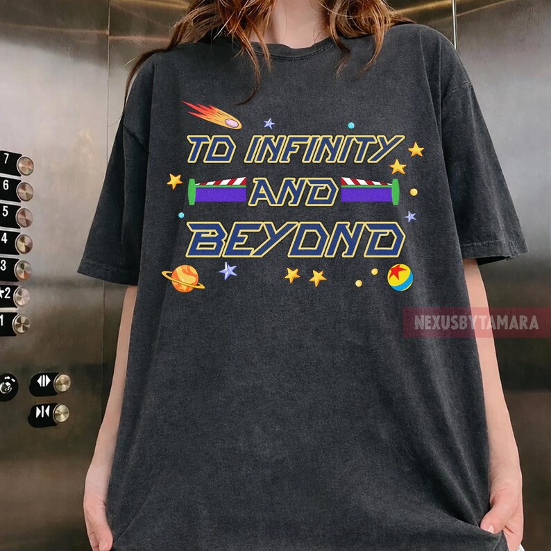 May include: Dark gray t-shirt with the phrase "TO INFINITY AND BEYOND" in yellow and blue. The design includes a shooting star, stars, and a planet. The shirt is a casual wear item.